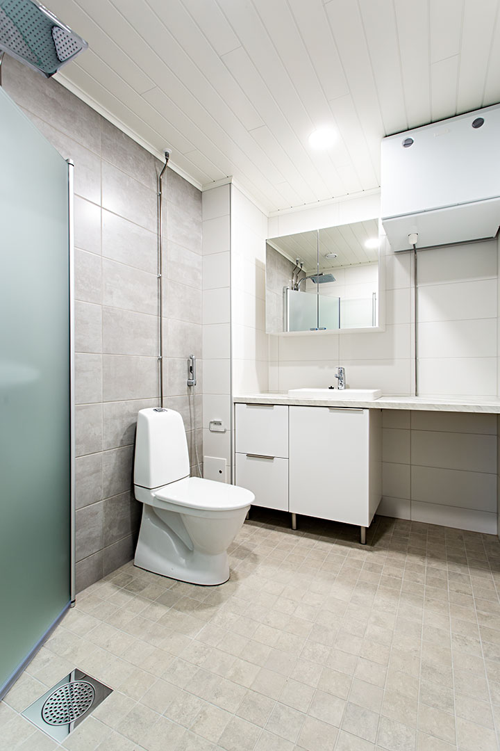 Kylpyhuone jossa vasemmalla lasitettu suihkukaappi, keskellä WC ja perällä lavuaari sekä peilikaappi. Lavuaarin alla valkoinen kaapisto.