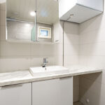Kylpyhuoneen lavuaari ja peilikaappi. Lavuaarin alla valkoiset kaapit. Vieressä taso, jonka ylä- ja alapuolella tyhjää tilaa.