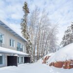 Talvinen ulkokuva kaksikerroksisesta talosta. Alakerroksen asuntojen kuistit rajattu tummalla puuseinällä.