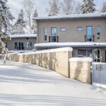 Talvinen ulkokuva kaksikerroksisesta asunnosta. Vaalea laudoitukset, aita sekä portti.
