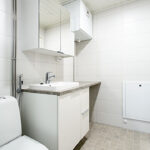 Kylpyhuone. Etualalla WC, sen vieressä lavuaari ja allaskaappi. Valkoiset kaapit lavuaarin alla.
